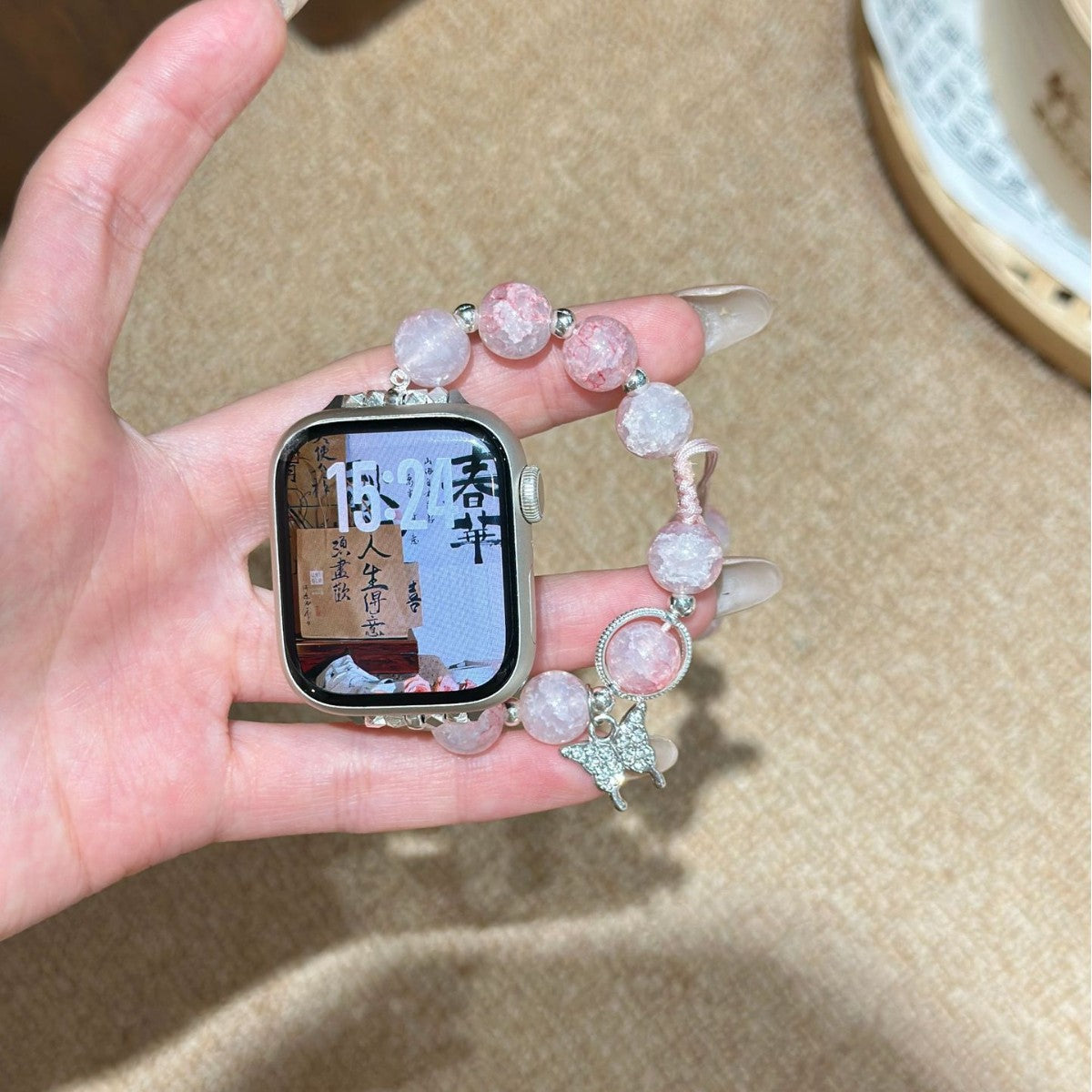 Pink beaded butterfly charm Apple Watch bracelet band held in hand