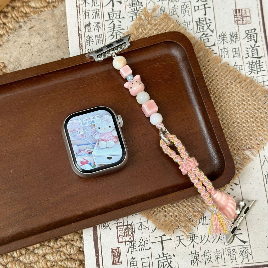Pink cat charm Apple Watch band laid open on wood tray