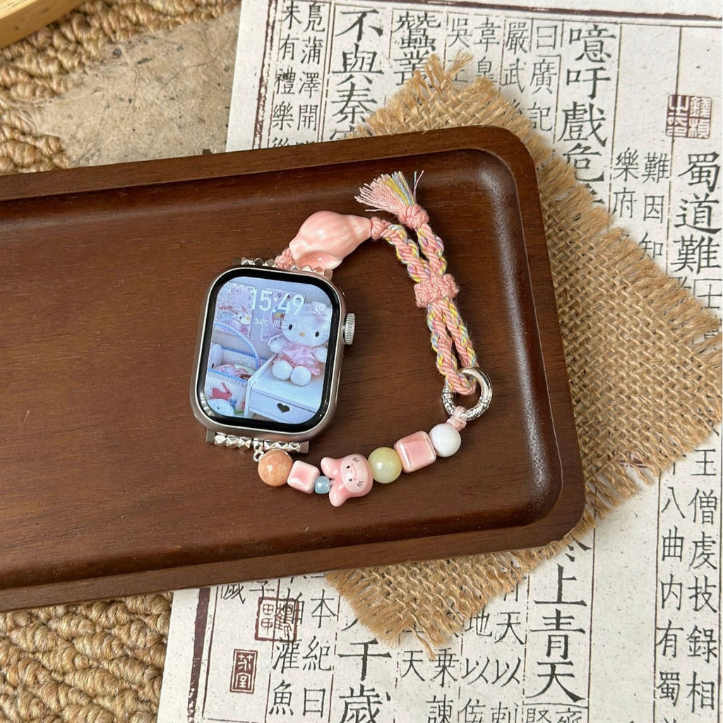 Pink braided Apple Watch band with pastel beads on wood tray