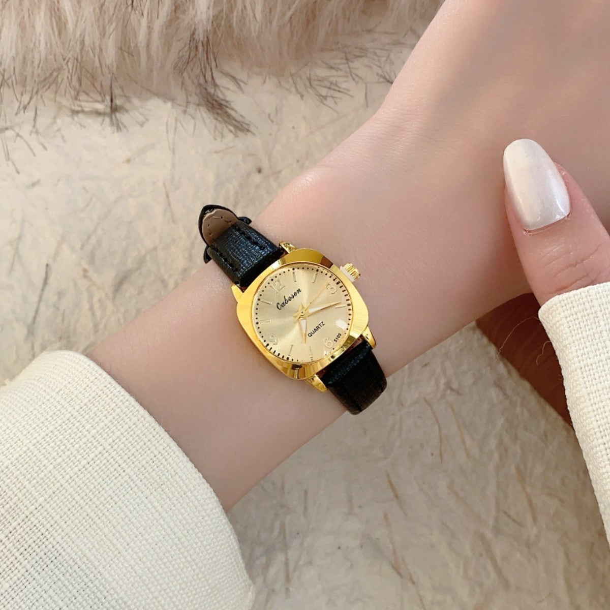 CABOSEN vintage small women's watch with gold-tone case, champagne dial and black leather-style strap on wrist