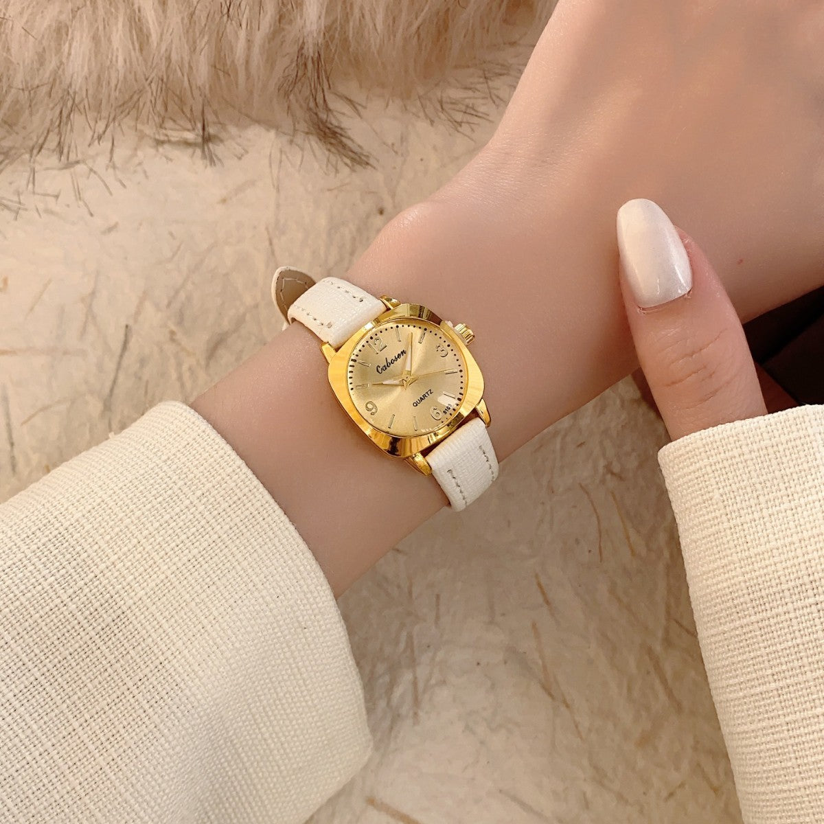 CABOSEN vintage small women's watch with gold-tone case, champagne dial and white leather-style strap on wrist