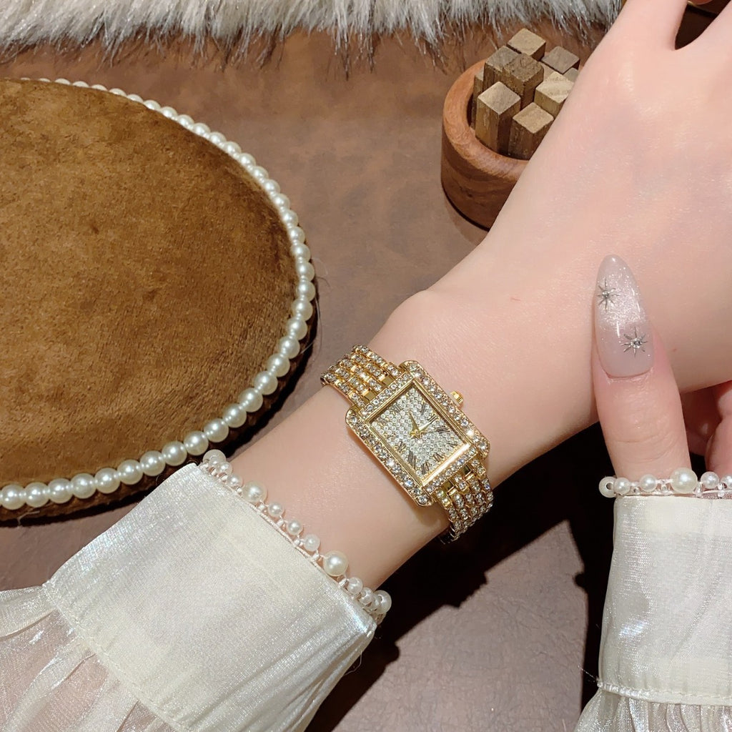 Crystal-style rectangular jewelry watch in gold tone worn on wrist