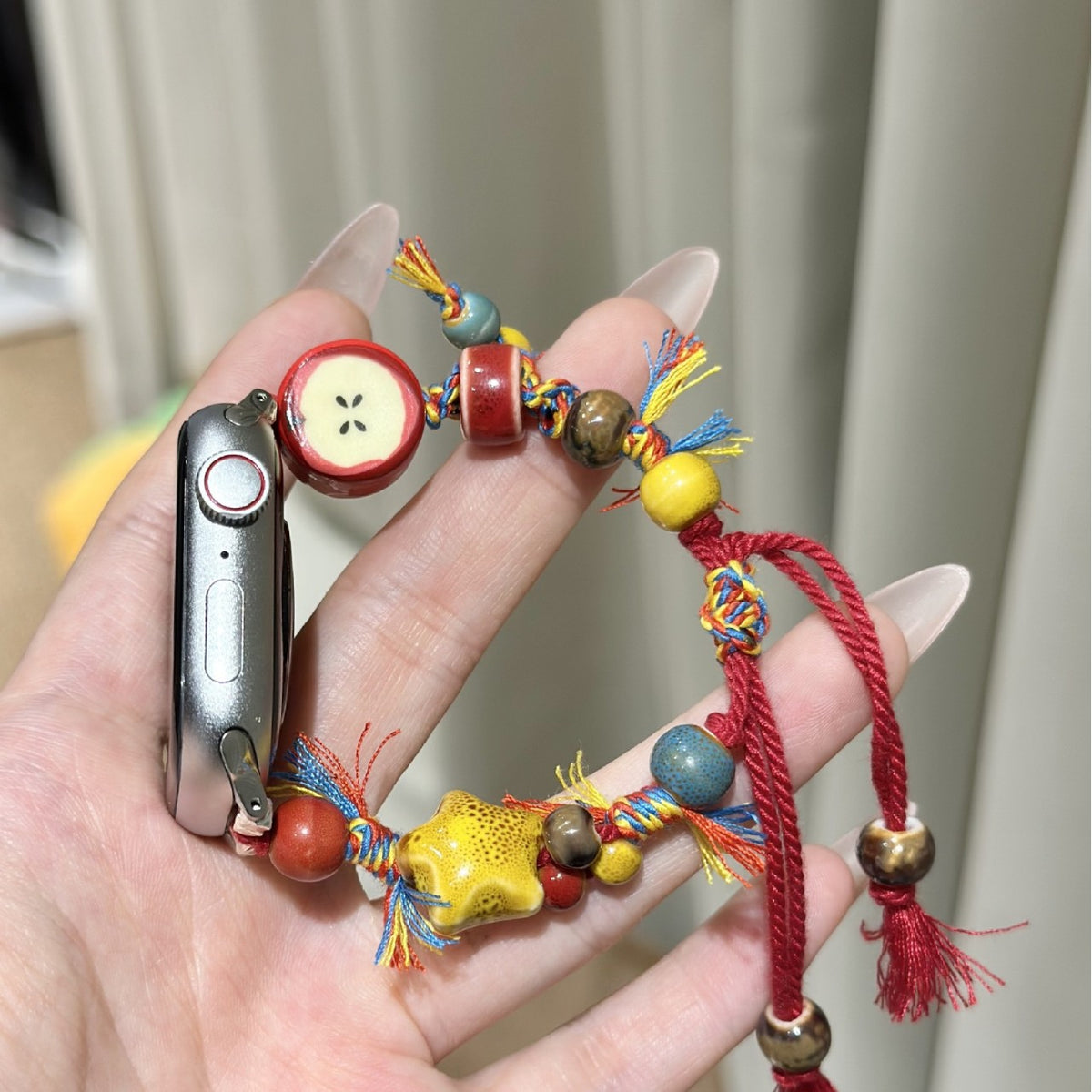 Red cord colorful apple charm Apple Watch bracelet band held in hand