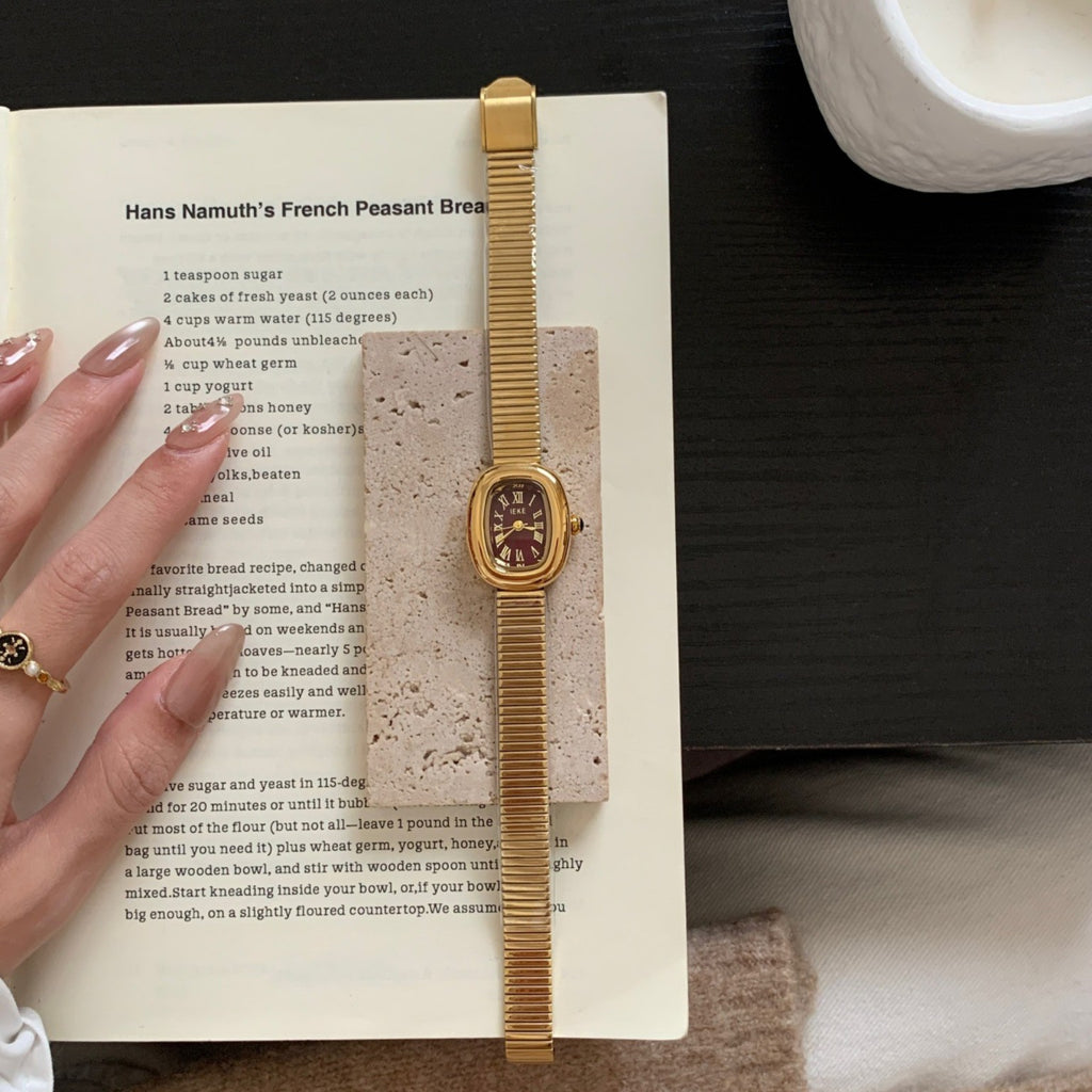 IEKE gold-tone women's oval watch with burgundy Roman numeral dial and expansion bracelet styled on a book