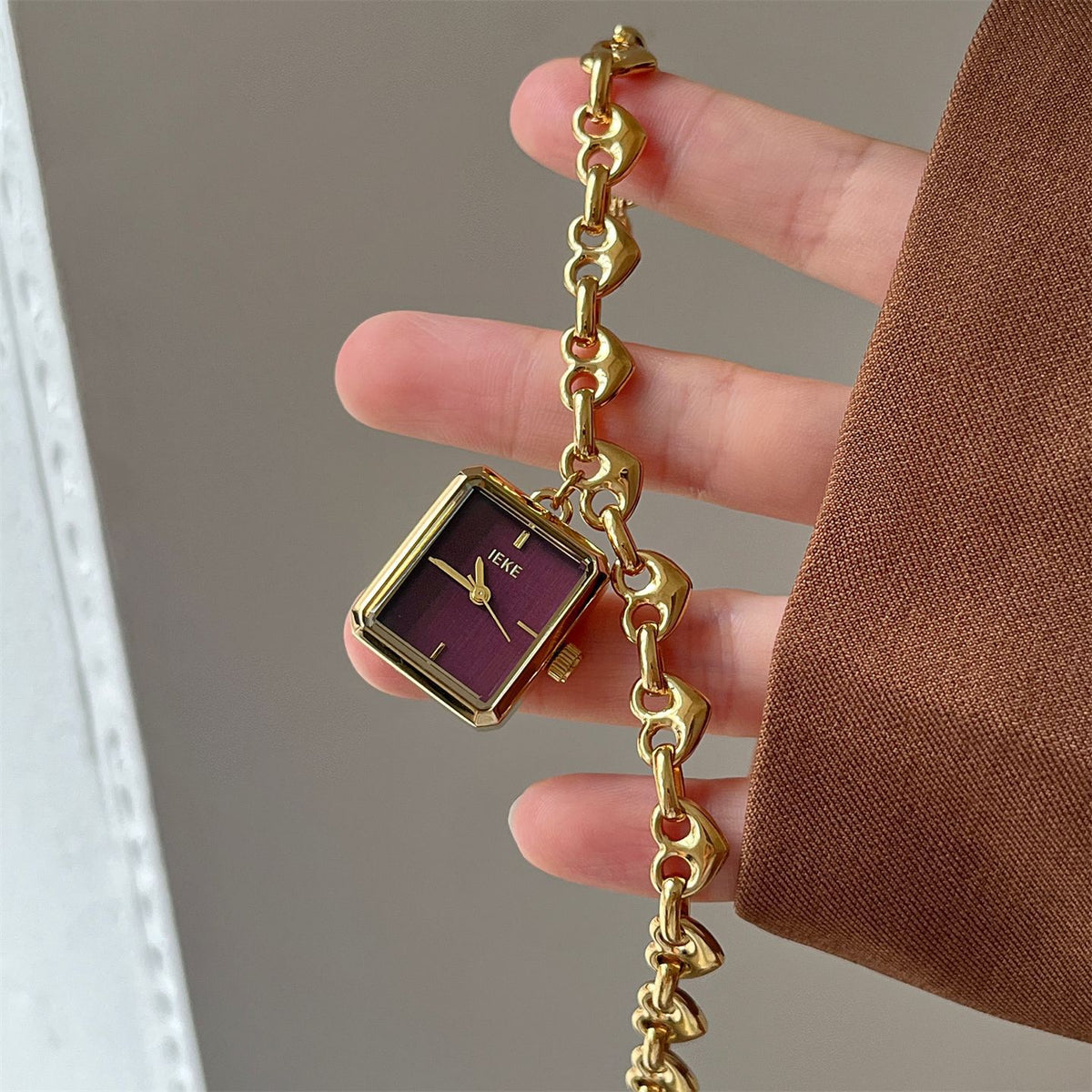 Close-up of IEKE gold-tone heart-link bracelet watch with plum dial