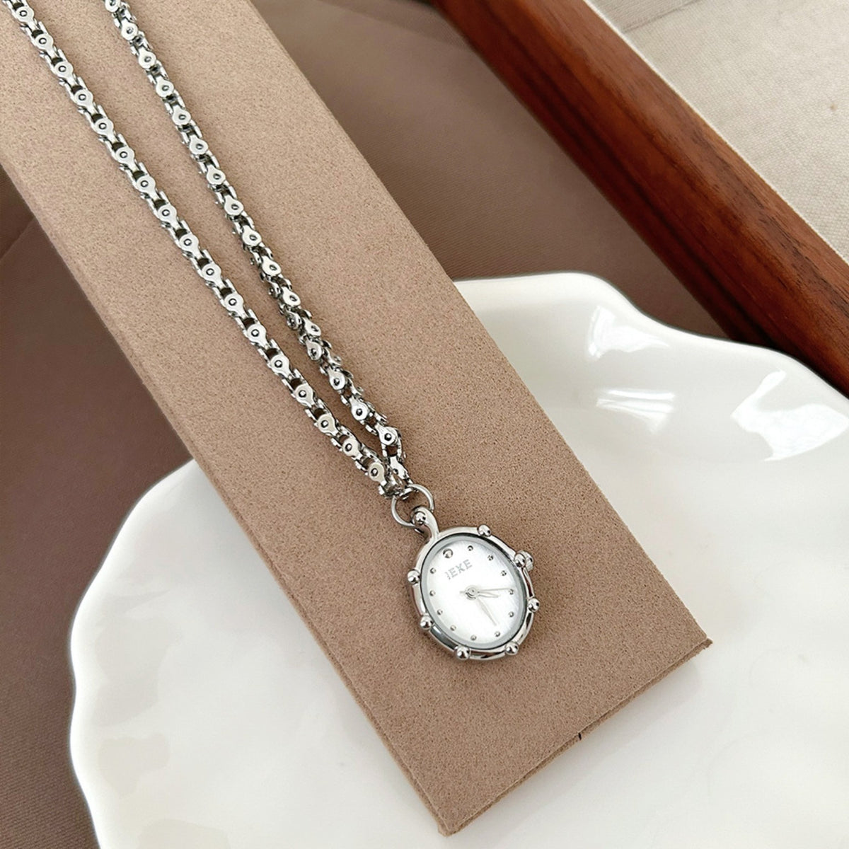 IEKE silver pendant necklace watch displayed on beige stand