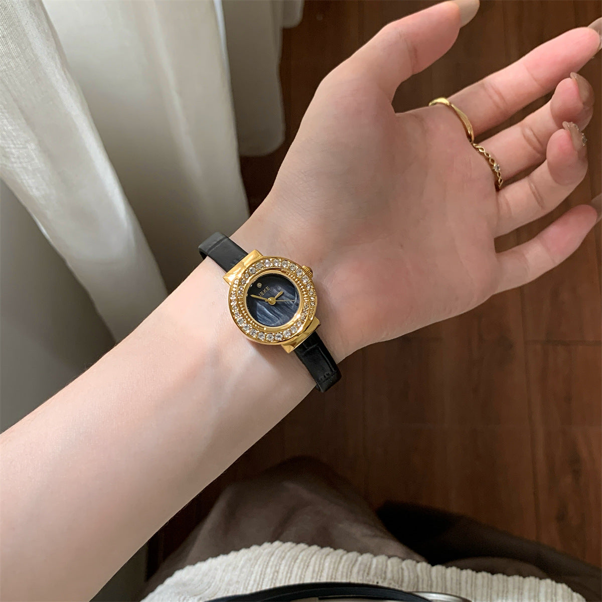 IEKE petite round crystal gold-tone watch with black strap worn on wrist