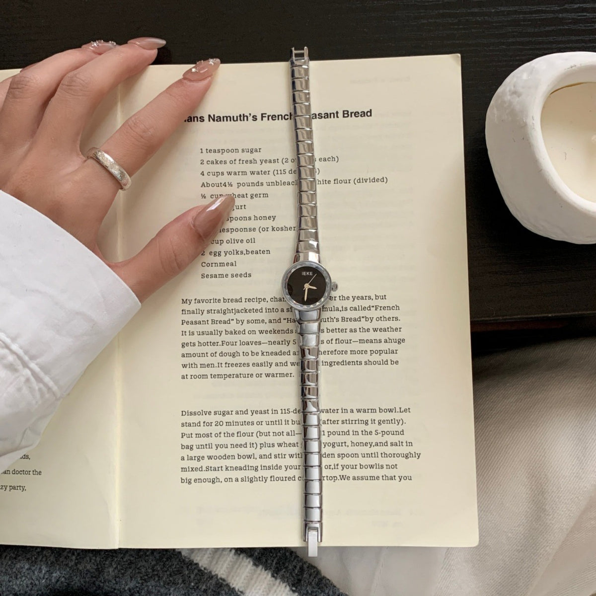 IEKE women's petite round silver-tone quartz watch with black dial styled on an open book