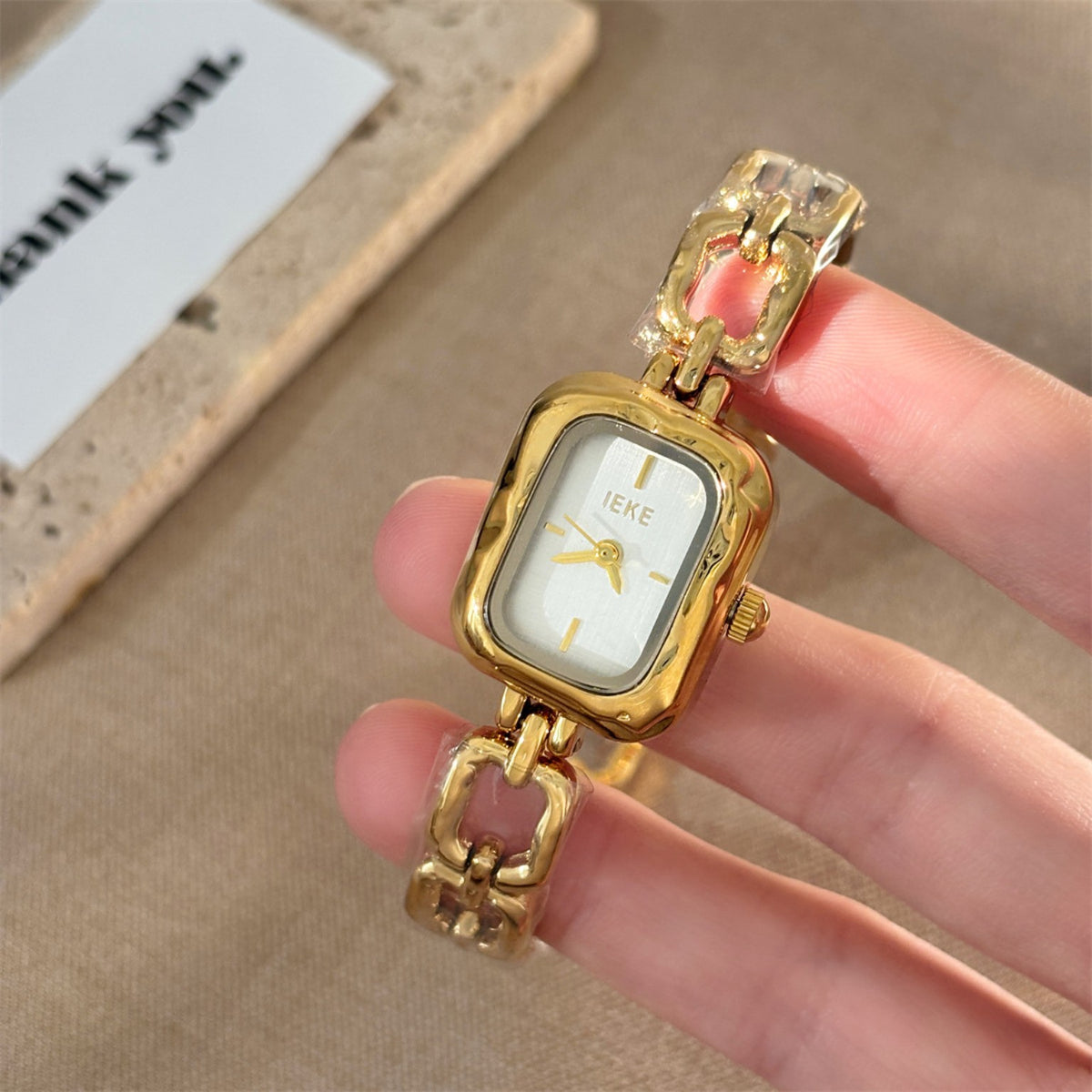 Handheld detail of IEKE women's sculpted link square bracelet watch in gold with ivory dial