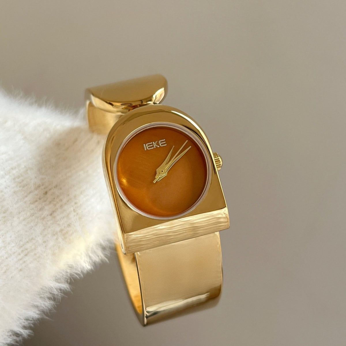 IEKE sculptural cuff bracelet watch in polished gold with amber dial
