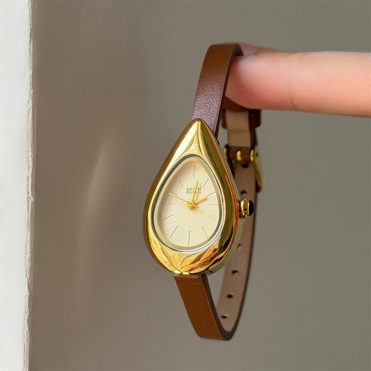 IEKE women's teardrop quartz watch with cream dial, brown strap and gold-tone case shown on wrist