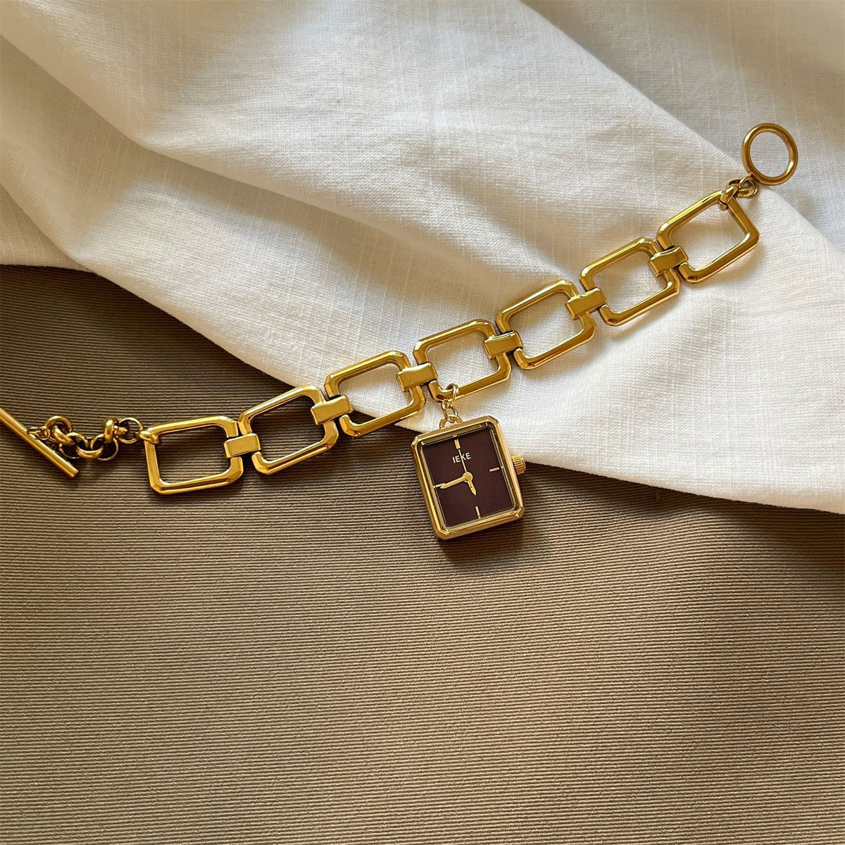 IEKE vintage charm bracelet watch with burgundy dial styled on neutral fabric