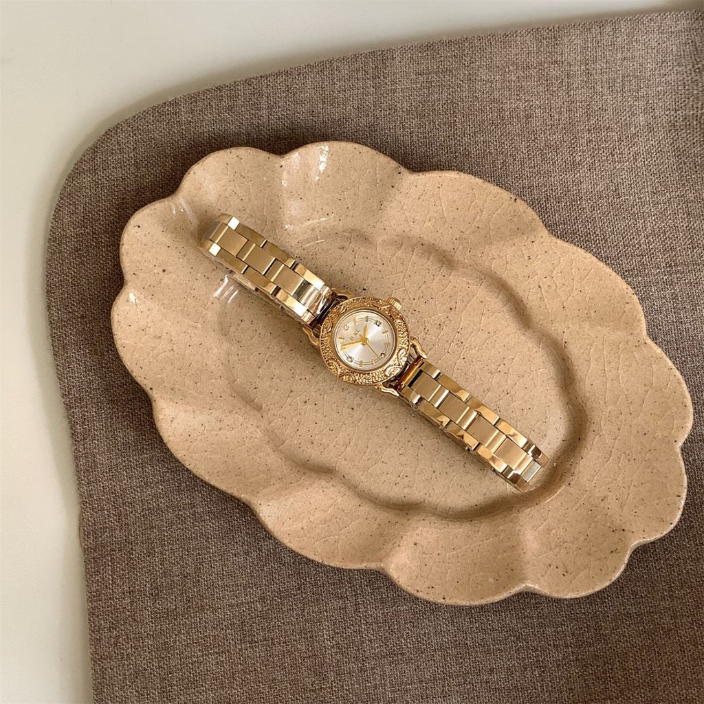 IEKE petite vintage women's quartz watch with cream dial and gold-tone bracelet on ceramic tray