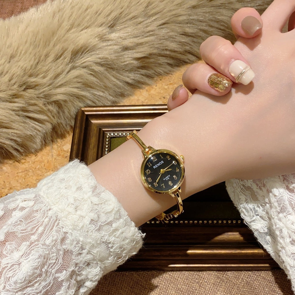 RENOS petite round bar-link bracelet quartz watch in gold tone with black dial worn on wrist