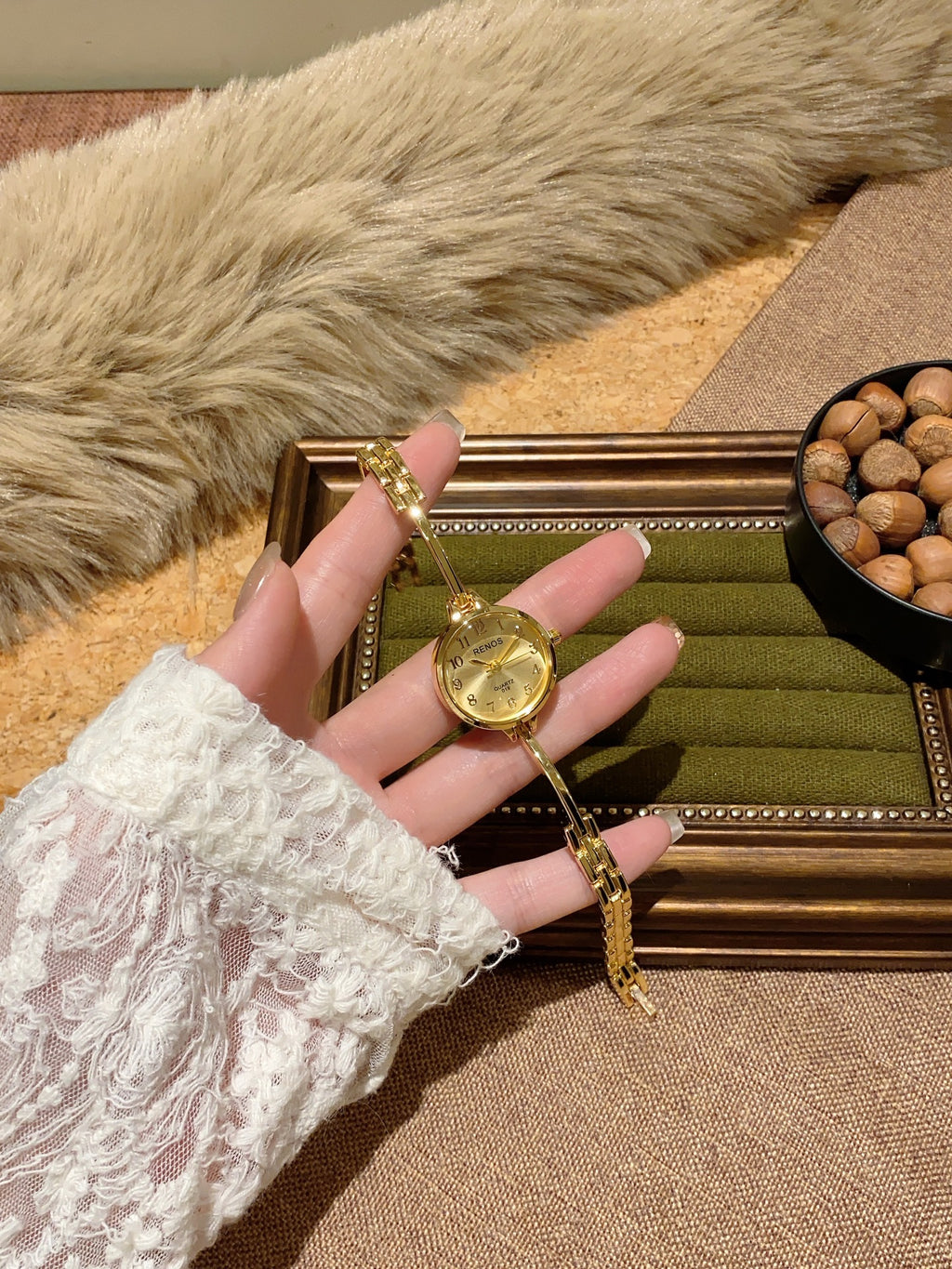 RENOS petite round bar-link bracelet quartz watch in gold tone with champagne dial held in hand