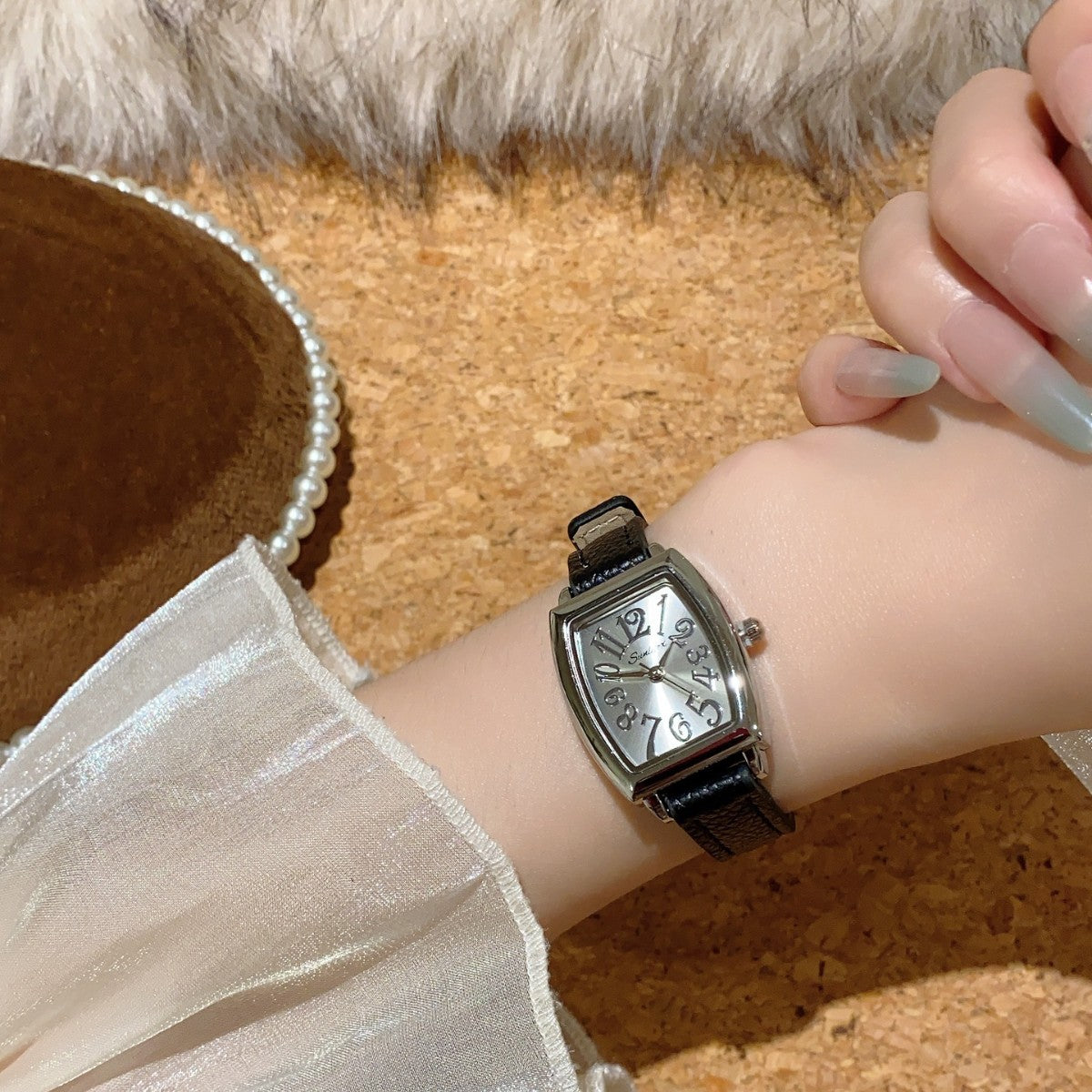 Vintage tonneau women's watch with white dial and black leather strap worn on wrist