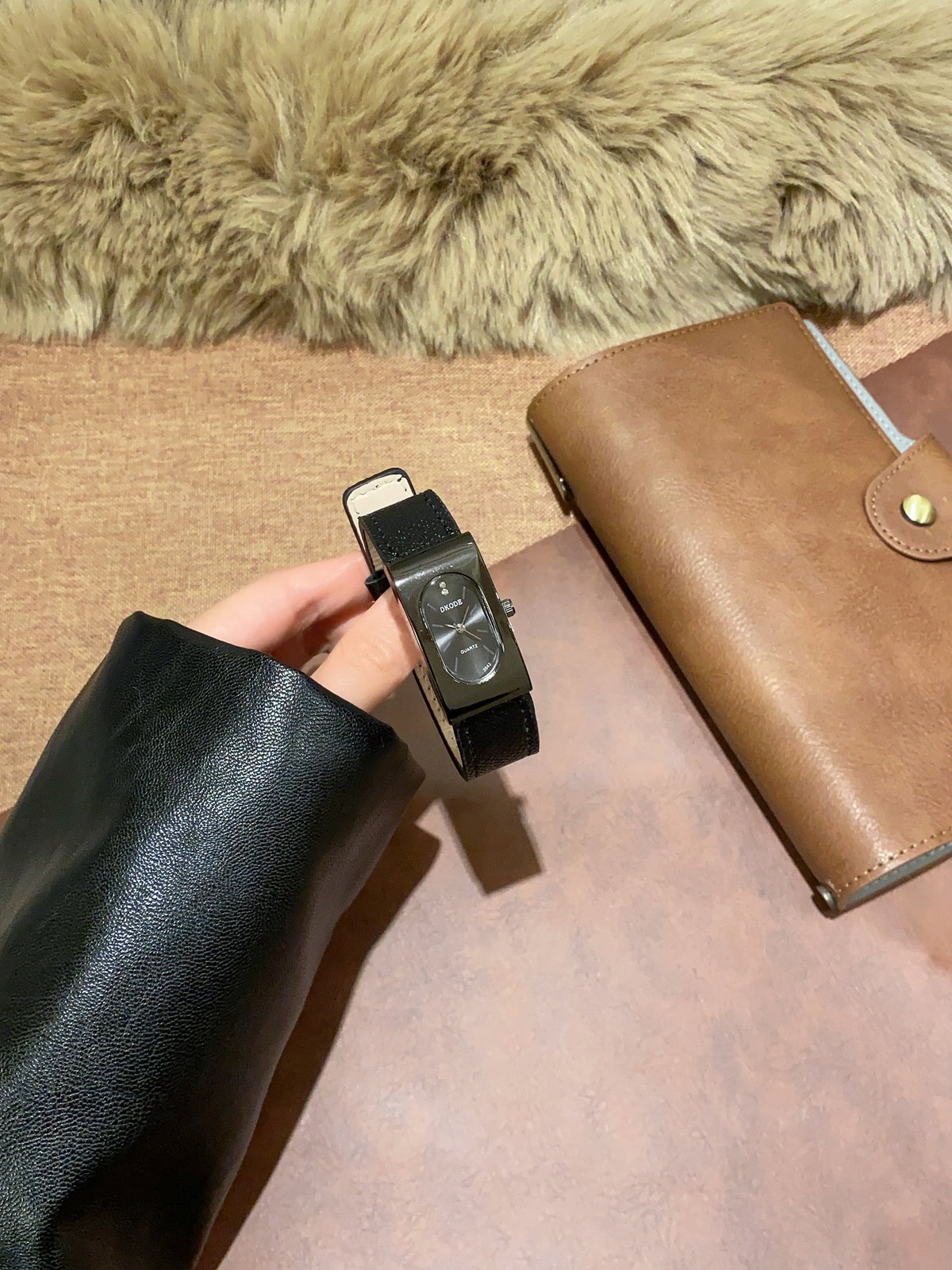 Vintage petite black tonneau women's quartz watch with black leather-style strap held in hand