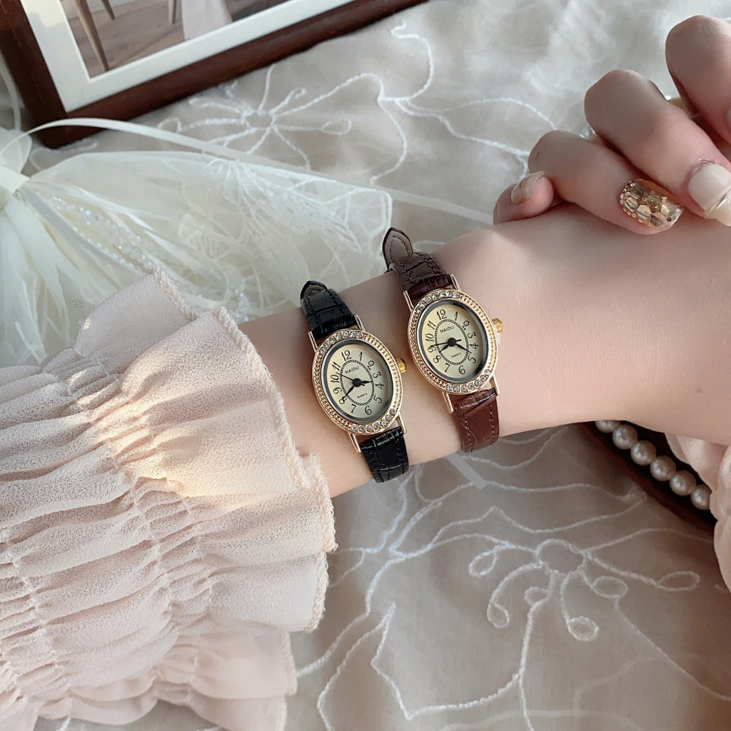 Gold-tone petite oval watches with black and brown straps styled on wrist