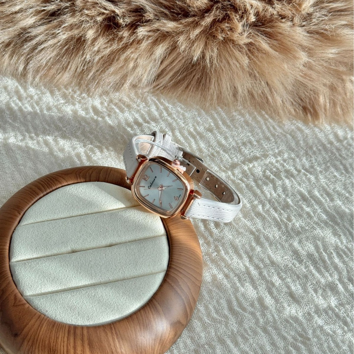 Vintage rose gold cushion case women's watch with ivory leather strap and silver dial, styled on a jewellery tray